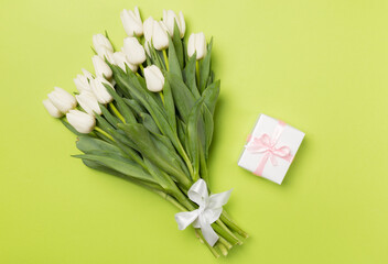 White tulip bouquet with gift on color background, top view