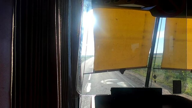 Sun shines brightly through curtain on driver's window of moving bus. Brightly shining sun in window of bus driving on road. View of road. Concept travel tourism transport transportation trip journey