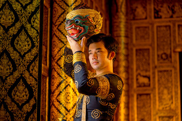 Fototapeta premium Asian man with traditional cloth relate to Khon or Thai classic masked with holding black monkey mask stand in front of windows of public building.