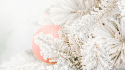 Christmas wallpaper. White theme. Branches of pine trees covered with snow with a red ball decoration hanging behind.
