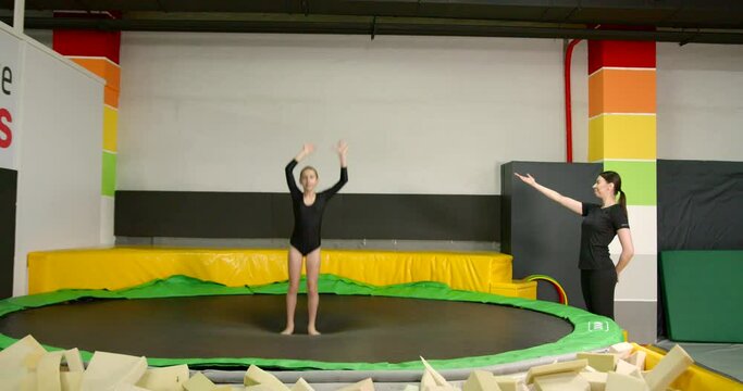 Little girl gymnast practicing on a trampoline with a coach