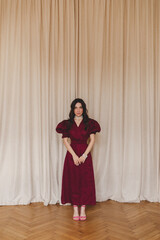 Girl in the cherry dress standing near blind. Women's health, sexuality. Portrait of a beautiful young woman in cherry dress with belt and puff sleeves. Sexy brunette woman look sensual.