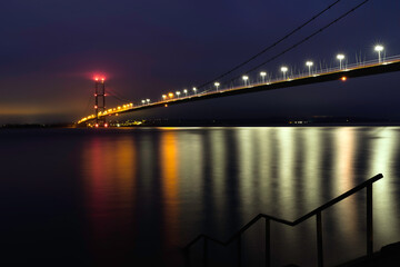 Humber bridge with bright lights across the esturary at pre-dawn. Hessle, UK.