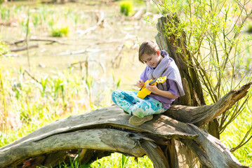Naklejka na ściany i meble boy playing ukulele on a log in nature on a sunny day