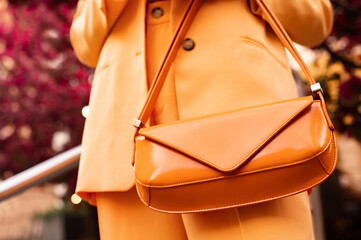 Street fashion details: woman wearing trendy yellow suit, carrying orange color faux patent leather baguette bag. Copy, empty space for text
