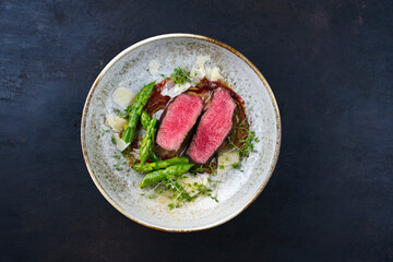 Gourmet barbecue dry aged angus beef steak with green asparagus and parmesan cheese in truffle mousse parfait and wild cherry relish cream served as top view in a Nordic design bowl with copy space