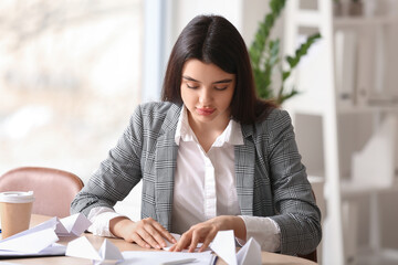 Young businesswoman making paper plane at table in office