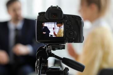 Fototapeta na wymiar Female journalist with microphone having an interview with man on camera screen in office, closeup