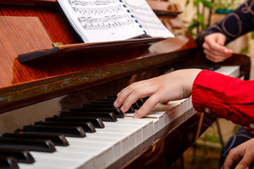 A child learns to play the piano in the lessons at a music school with a teacher.