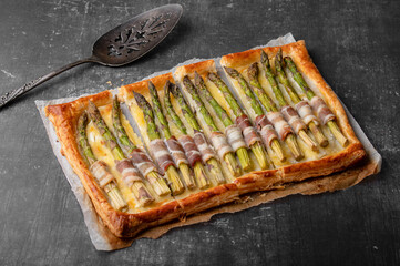 Puff pastry tart with green asparagus and bacon. Asparagus pie with cheese and bacon on a light background