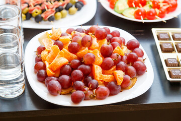 Fruits and canap s with olives and ham cheese on white buffet plates.
