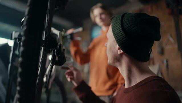 Dad and son work in the garage: dad teaches son how to fix a bike. Dad spins the wheel to see if the bike is working