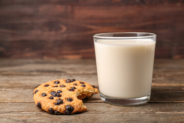 Glass of milk and bitten cookie with chocolate chips on wooden background