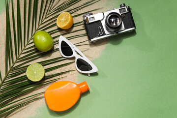 Palm leaf with citrus fruits, sunglasses, sunscreen cream, photo camera and sand on green background