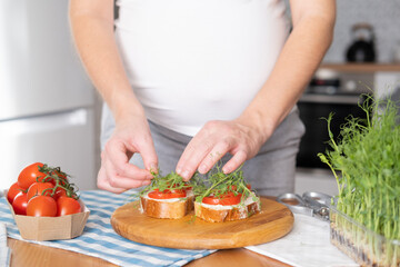 Obraz na płótnie Canvas Pregnant young woman preparing healthy sandwiches with microgreens and vegetables. Food rich in fiber