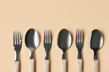 Stainless steel forks and spoons with plastic handles on beige background