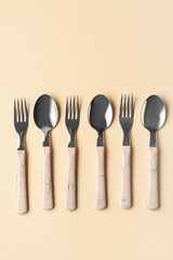 Stainless steel forks and spoons with plastic handles on beige background