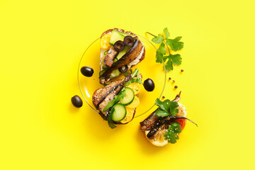 Plate of tasty sandwiches with canned smoked sprats on yellow background