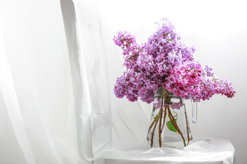 Vase with lilac flowers on chair in light room, closeup