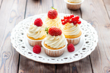 Vanilla cupcakes decorated with fresh strawberry, raspberry and red currant on rustic wooden background