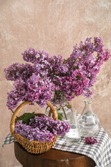 Vases with lilac flowers and basket on table in room