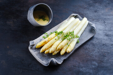 White asparagus glazed with sauce hollandaise and cress served as close-up on a design tray with text space