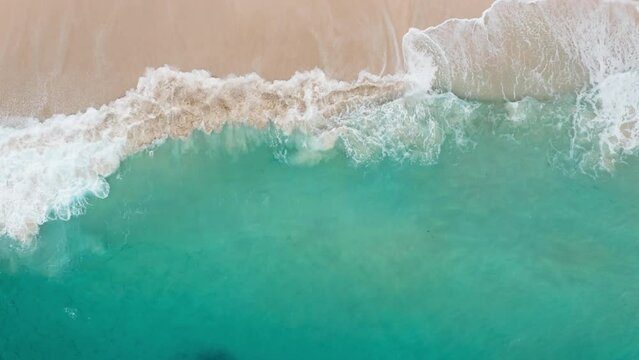 Drone view of beautiful footage while turquoise raging sea waves breaking on sandy coastline. Aerial top shot of beach with strong power ocean water and foam waves. Paradise. Big swell.
