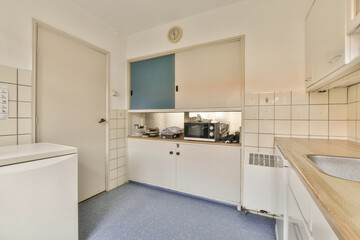 a kitchen with blue tile on the floor and white cupboards in the wall behind it is an open door that leads to a