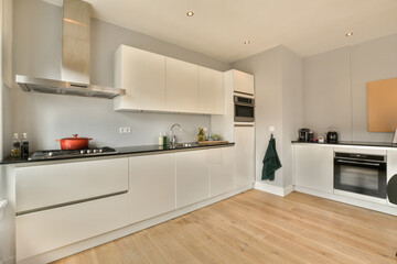 a kitchen with white cabinets and wood flooring in the middle of the room there is an oven on the wall