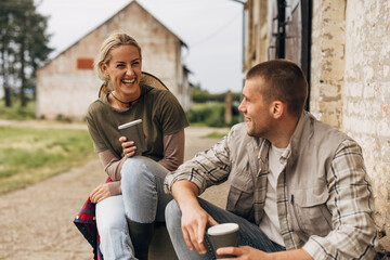 A woman and a man sit outside on the stairs and laugh while talking.