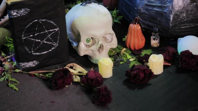 Close-up, black book with pentagram, skull and cauldron on the table with witchcraft ingredients. Halloween witch altar concept. Smooth camera movement, selective focus.