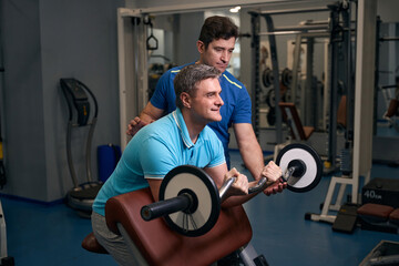 Adult man doing biceps exercise guided by personal trainer