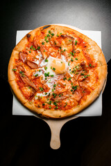 Pizza with bacon, egg, cheese and onion close-up on a wooden board on dark table