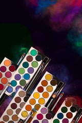 Bright eye shadow, blush brushes, explosion of multicolored powder dust on black background. Highly...