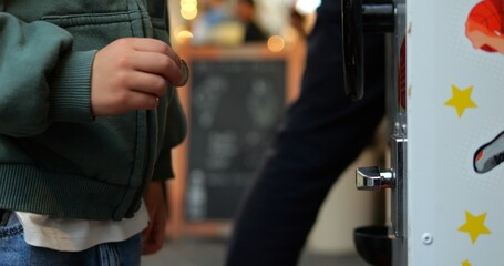 Five year old child holds coin want to insert into game or vending machine. Closeup shot of preschool kid hand ready to pay in toy machine.