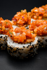 Freshly made appetizing sushi roll with sesame and caramelized onions on black background