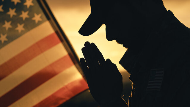 Silhouette of American soldier praying for memorial day against the flag outdoor