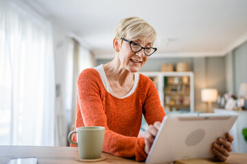 One senior blonde woman use digital tablet for video call at home