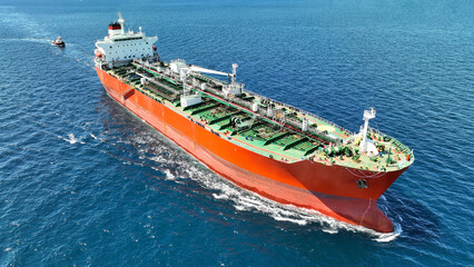 Aerial drone photo of huge crude oil tanker assisted by tug boat cruising open ocean deep blue sea