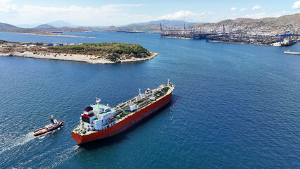 Aerial drone photo of huge crude oil tanker assisted by tug boats cruising near container terminal...