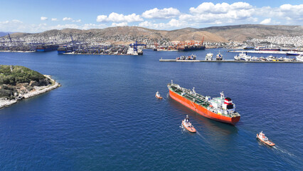 Aerial drone photo of huge crude oil tanker assisted by tug boats cruising near container terminal of Perama, Piraeus, Attica, Greece