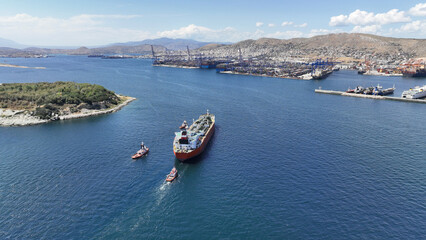 Aerial drone photo of huge crude oil tanker assisted by tug boats cruising near container terminal...