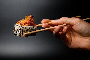 side view of one piece of tasty roll with caramelized onion, raw fish, sesame and rice in hand