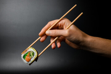 Man's hand holding wooden chopsticks with one piece of Philadelphia sushi roll