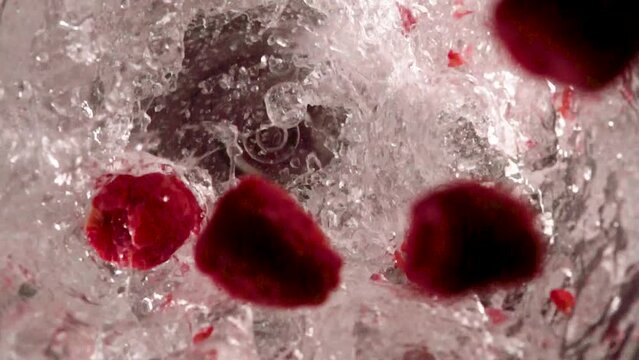 Raspberries falling into water in a blender in slow motion