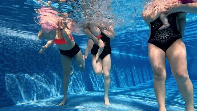 Little cute baby girls, children jumping into water, swimming underwater in swimming pool with her caring, loving mother. Family activity. Concept of sport, healthy and active lifestyle, childhood