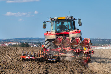 Red tractor on field at plowing and harrowing farm land soil in summer nature under blue sky....