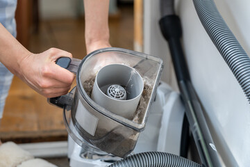 Woman opening dust filter out of vacuum cleaner at home. Hoover container full of dirt, fur, pet...