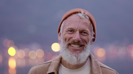 Happy older bearded man standing in nature park outdoors and laughing. Smiling active mature senior traveler looking at camera advertising camping tourism. Close up face front portrait.