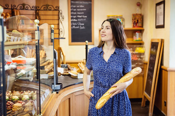 Young attractive woman buying french baguette in bakery shop. A customer standing near a showcase...